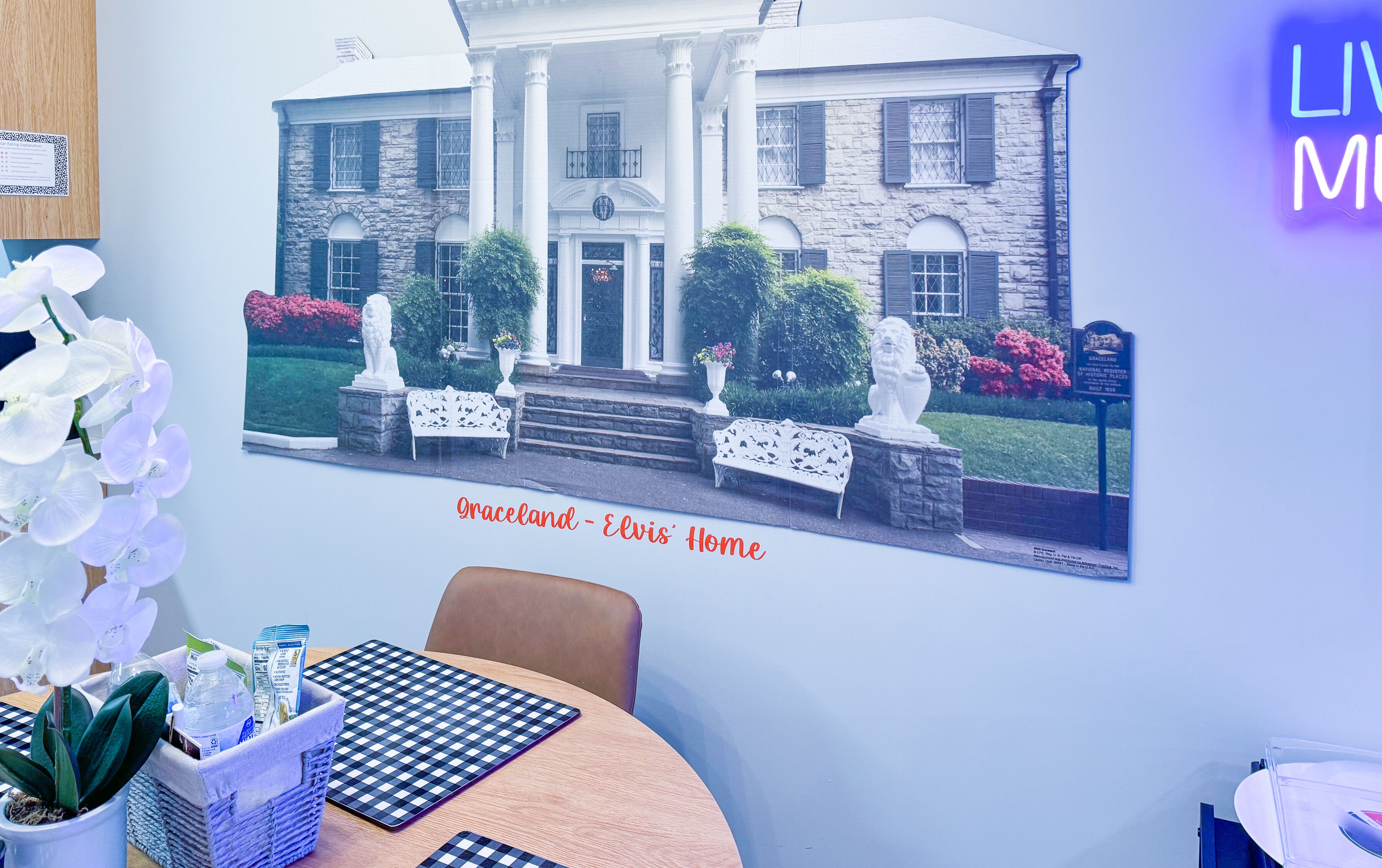 A framed picture of a historic building labeled "Graceland - Elvis' Home" with a checkered table and chairs in the foreground.
