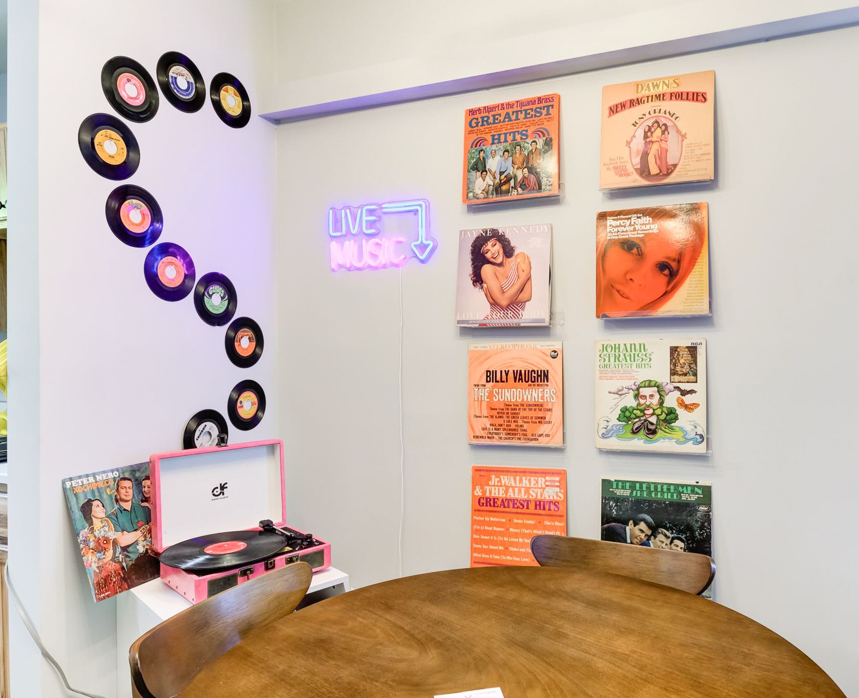 A room with a wooden table, vinyl records on the wall, and a neon sign that reads "LIVE MUSIC".