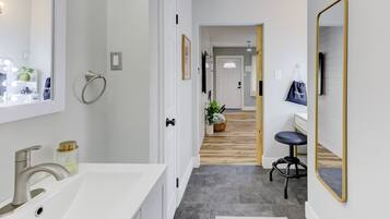 A modern bathroom with a white sink, a mirror, and a wooden floor leading to a hallway.