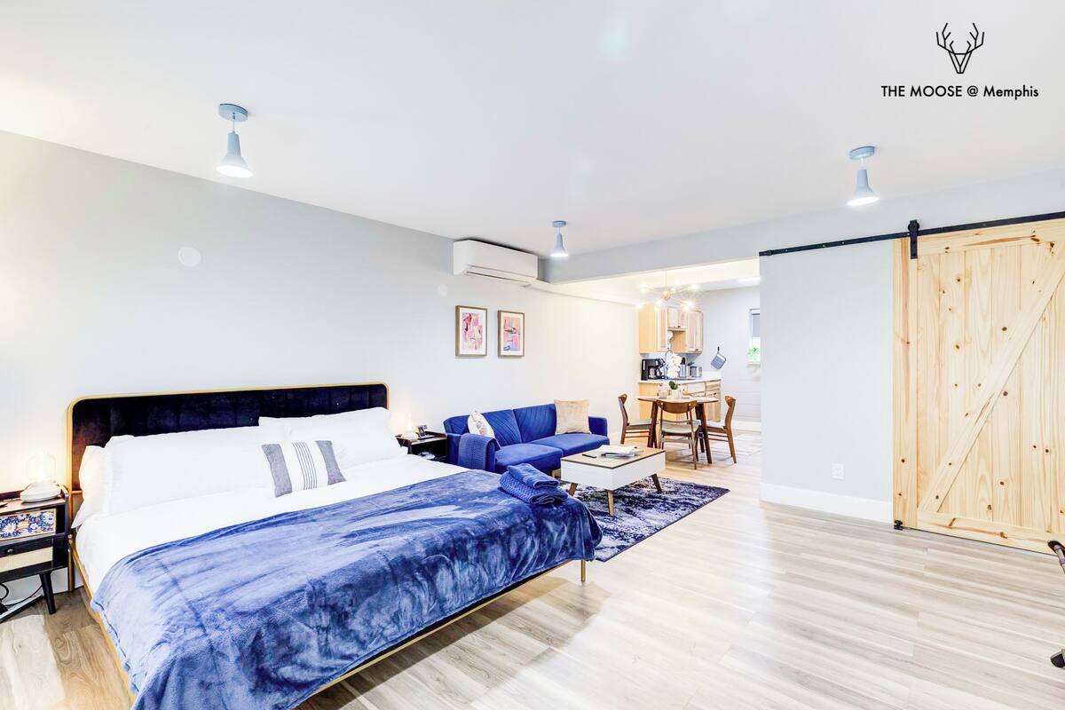 Una habitación de hotel moderna con cama, sofá azul, zona de comedor y puerta de madera.