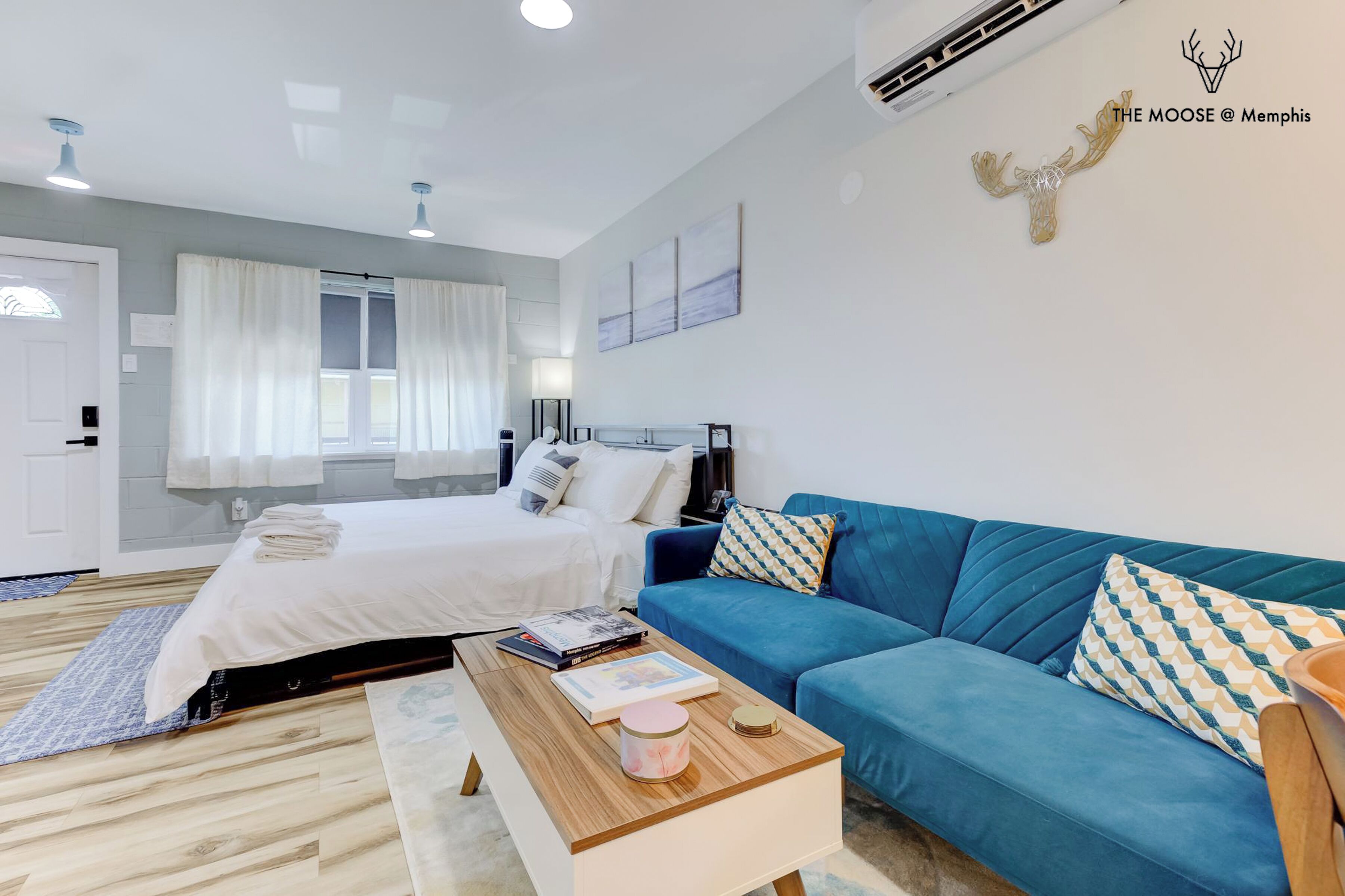 A modern bedroom with a bed, a blue sofa, a wooden coffee table, and a wall-mounted air conditioner.