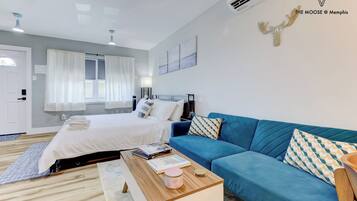 A modern bedroom with a bed, a blue sofa, a wooden coffee table, and a wall-mounted air conditioner.