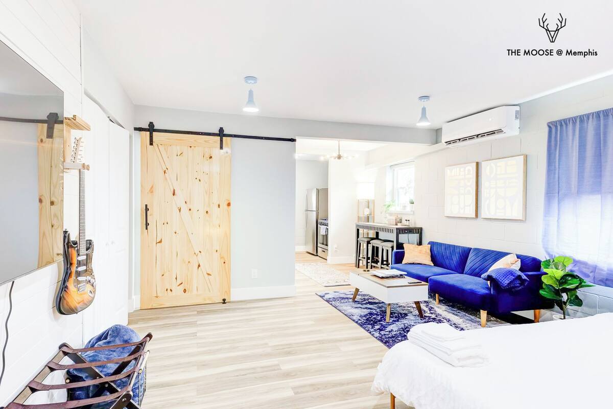 Una sala moderna con un sofá azul, una puerta corredera de madera y una guitarra en la pared.