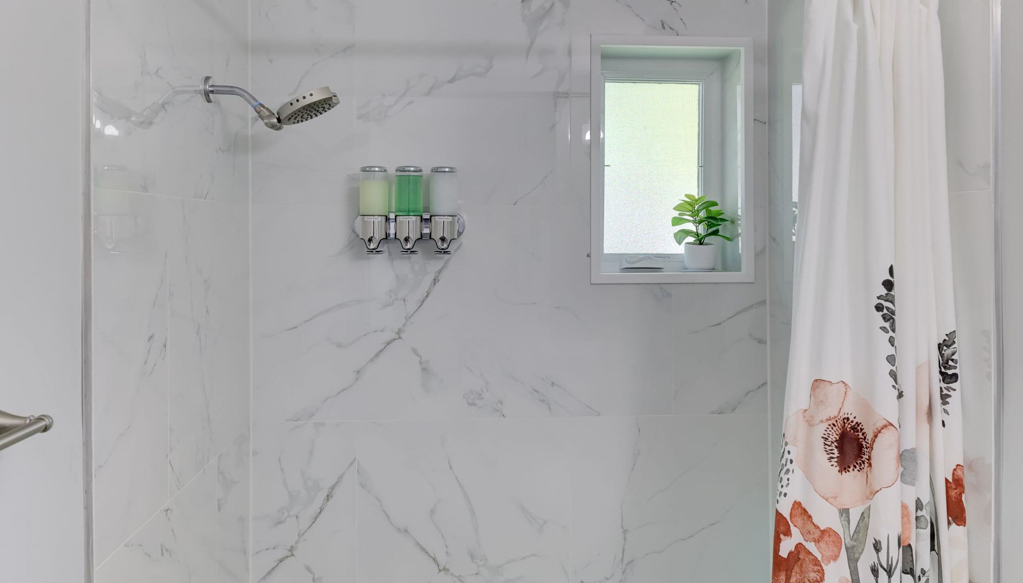 A bathroom with a shower, a small window, and two bottles of shampoo.