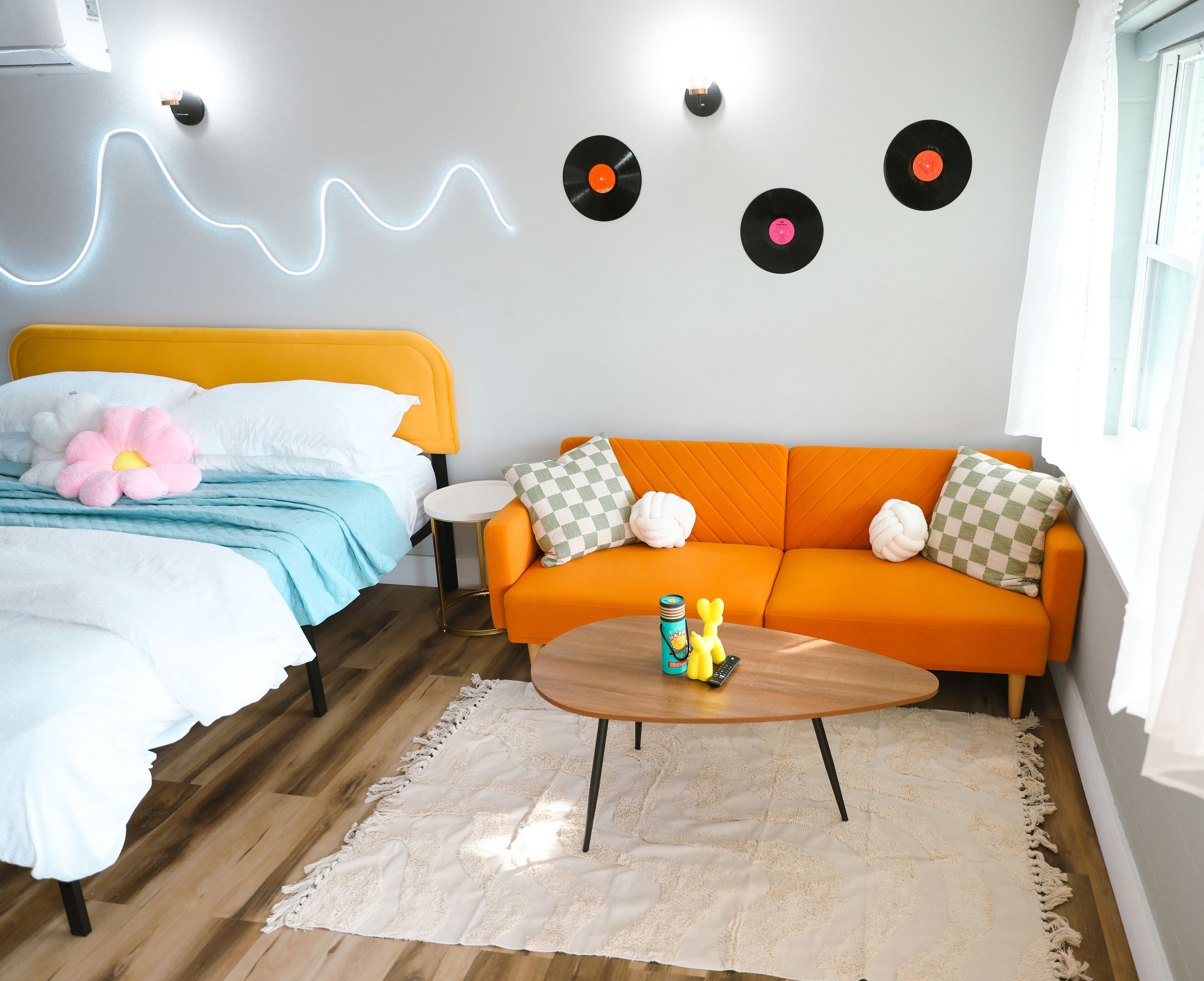 A modern bedroom with a bed, an orange sofa, a coffee table, and wall-mounted record players.