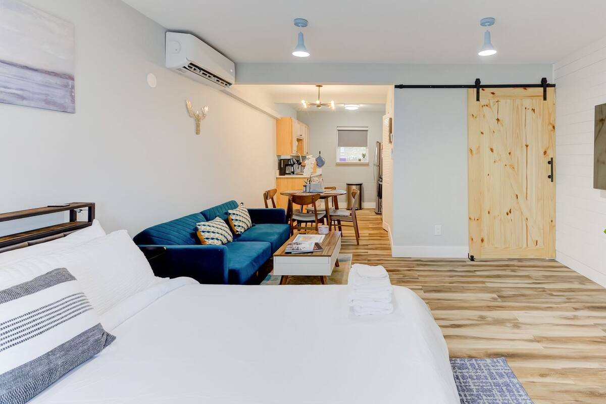 Una habitación de hotel moderna con una cama, un sofá azul, una zona de comedor y una puerta corredera de madera.