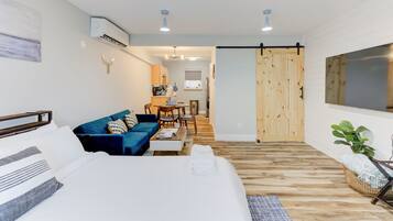 A modern hotel room with a bed, a blue sofa, a dining area, and a wooden sliding door.