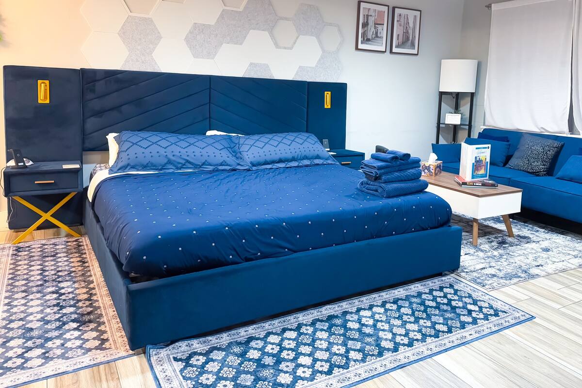 Una habitación de hotel moderna con una cama grande, un sofá azul, una mesita de noche y una lámpara.