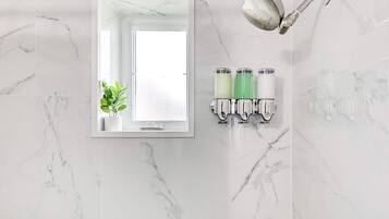 A bathroom with a marble wall, a mirror, a showerhead, and two soap dispensers.