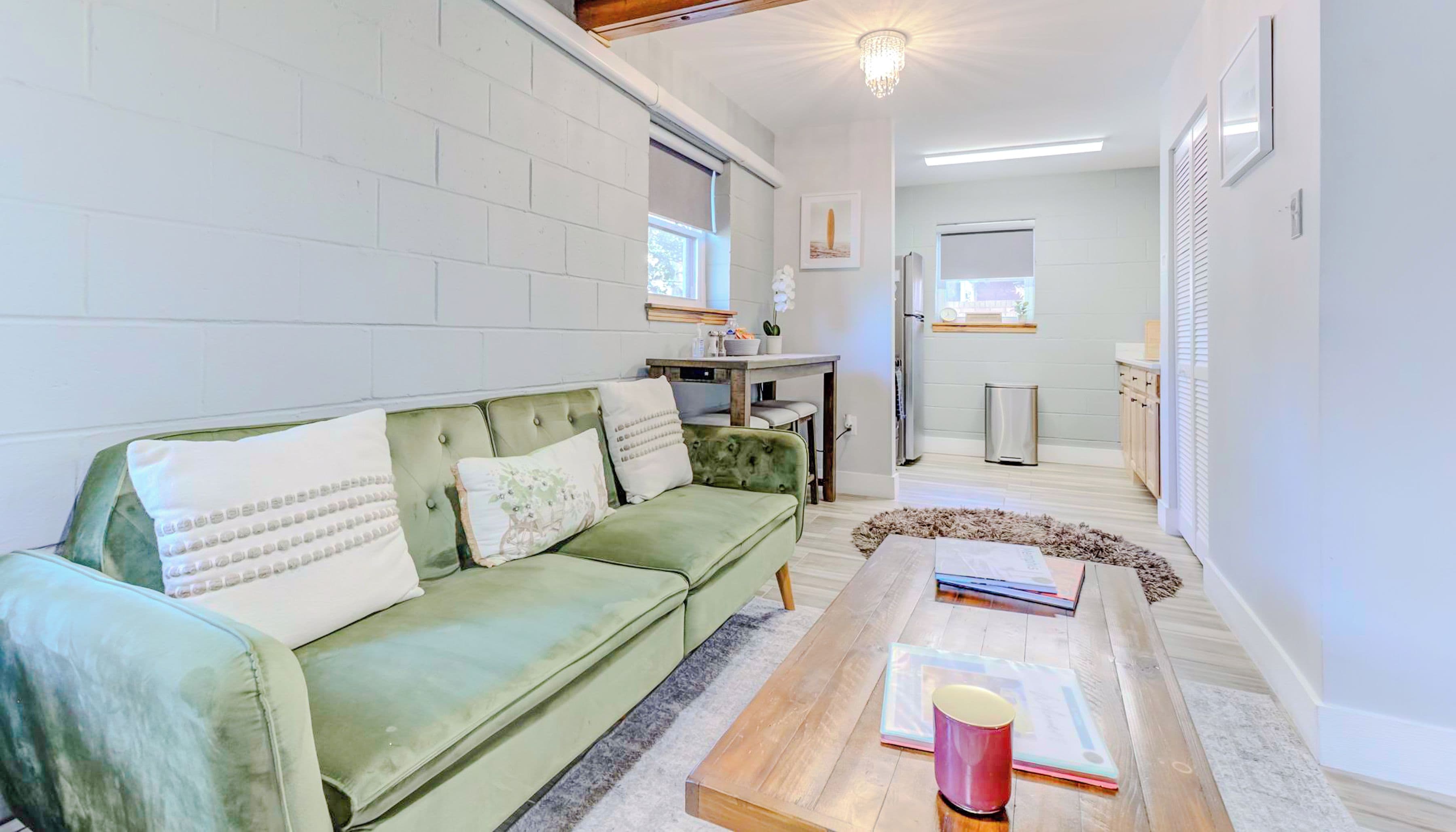 A cozy living room with a green sofa, a wooden coffee table, and a white brick wall.