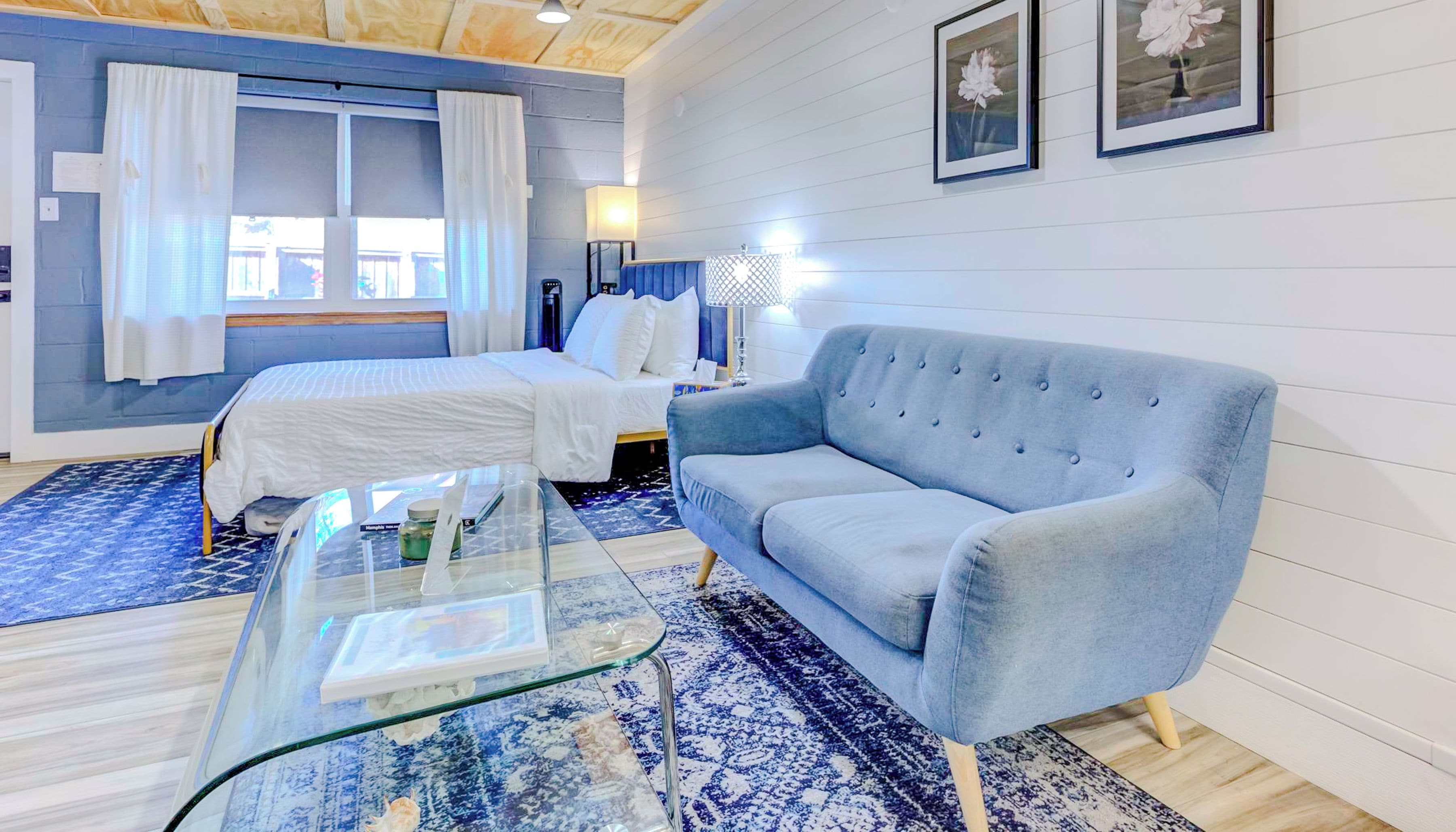 A bedroom with two beds, a blue sofa, a glass coffee table, and a patterned rug.
