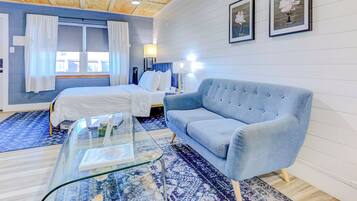 A bedroom with two beds, a blue sofa, a glass coffee table, and a patterned rug.