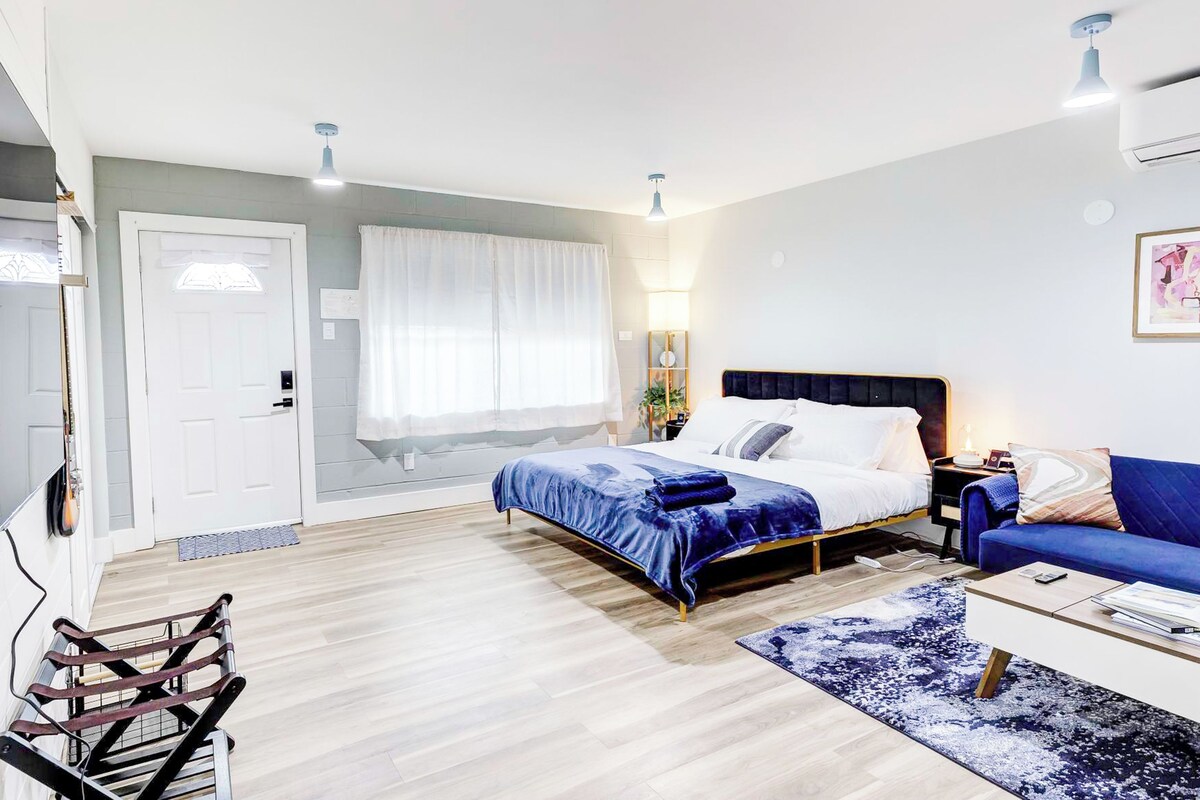 Un dormitorio moderno con una cama, mesitas de noche, un sofá azul y una pequeña mesa.