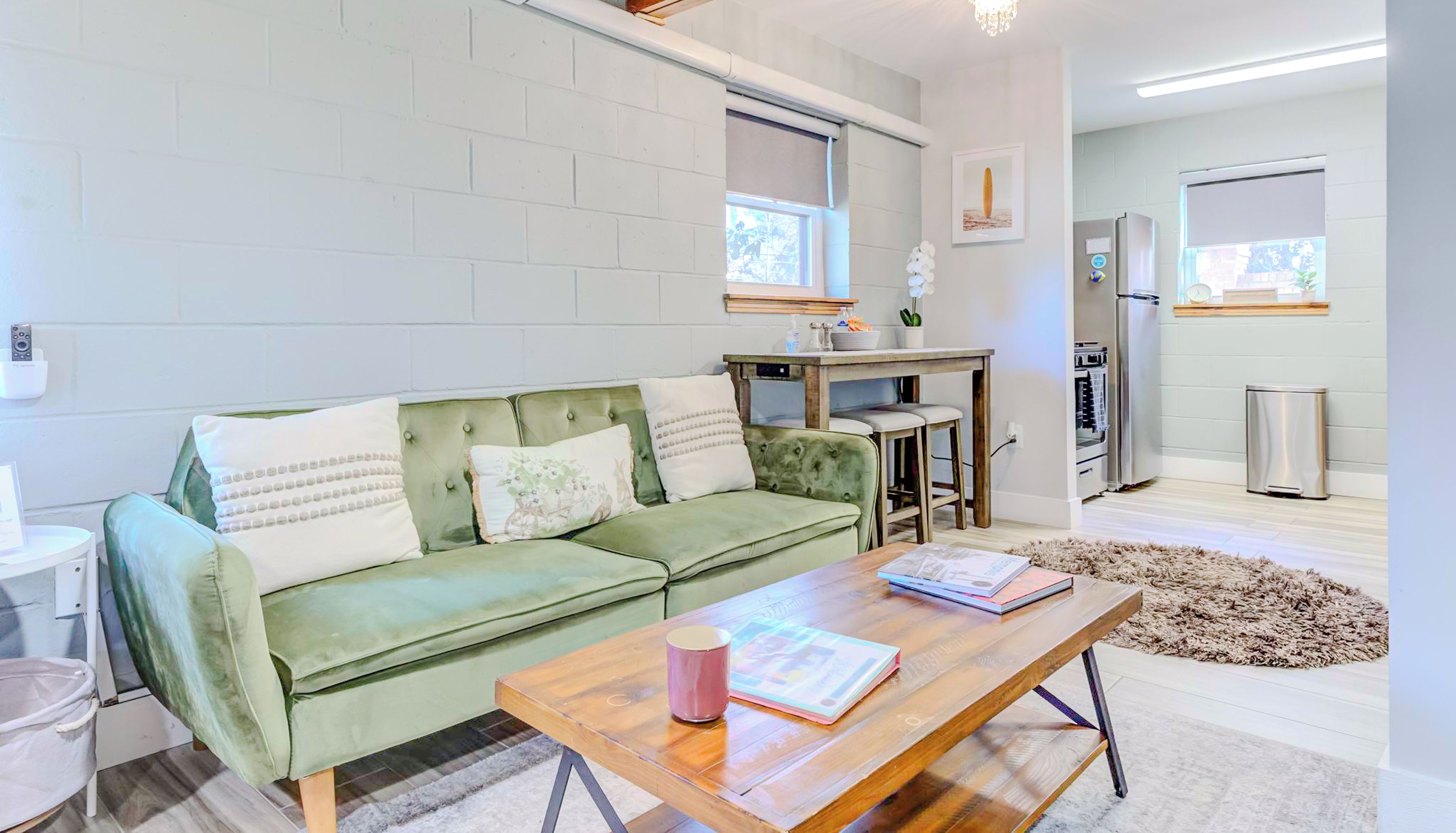 Een moderne woonkamer met een groene bank, een houten salontafel en een keuken met een koelkast en een spoelbak.