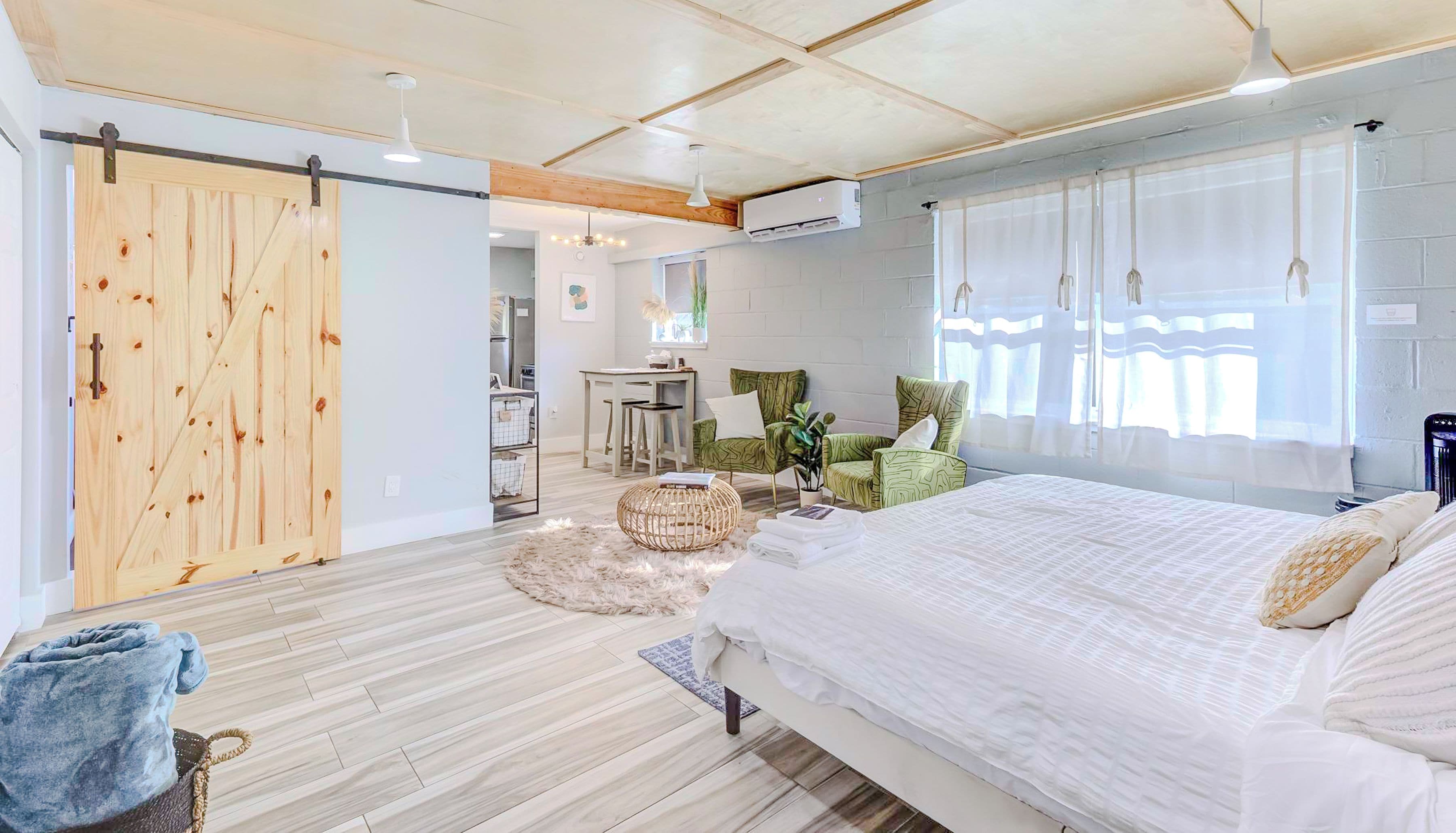 A modern bedroom with a large bed, a wooden door, a desk, and a green chair.