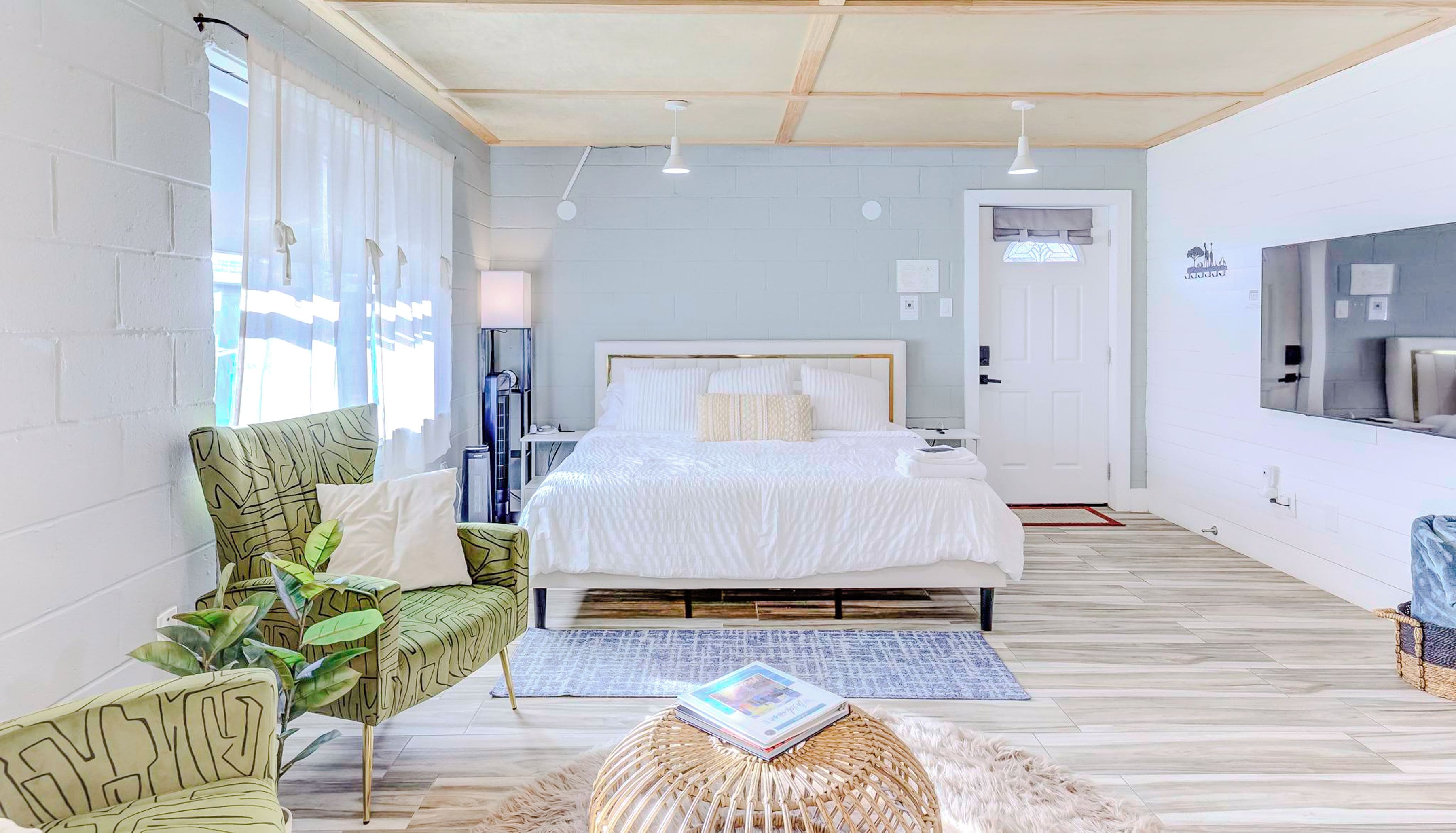 Un dormitorio moderno con una cama grande, un sillón verde estampado y una mesita redonda con una revista.