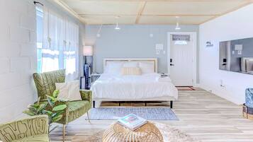 Un dormitorio moderno con una cama grande, un sillón verde estampado y una mesita redonda con una revista.