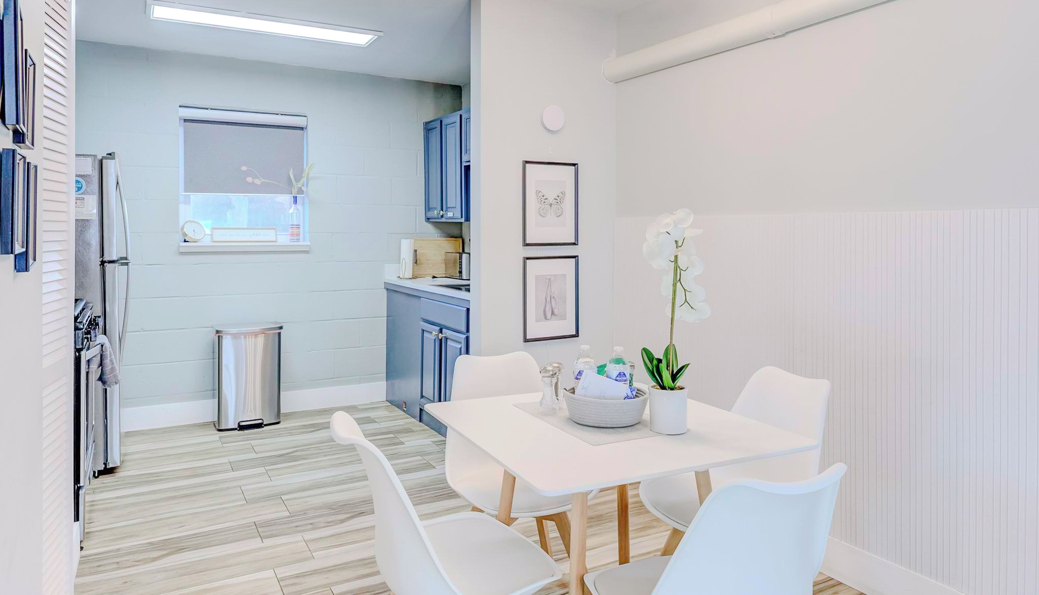 Una cocina moderna con armarios blancos, una ventana y un comedor con mesa y sillas blancas.