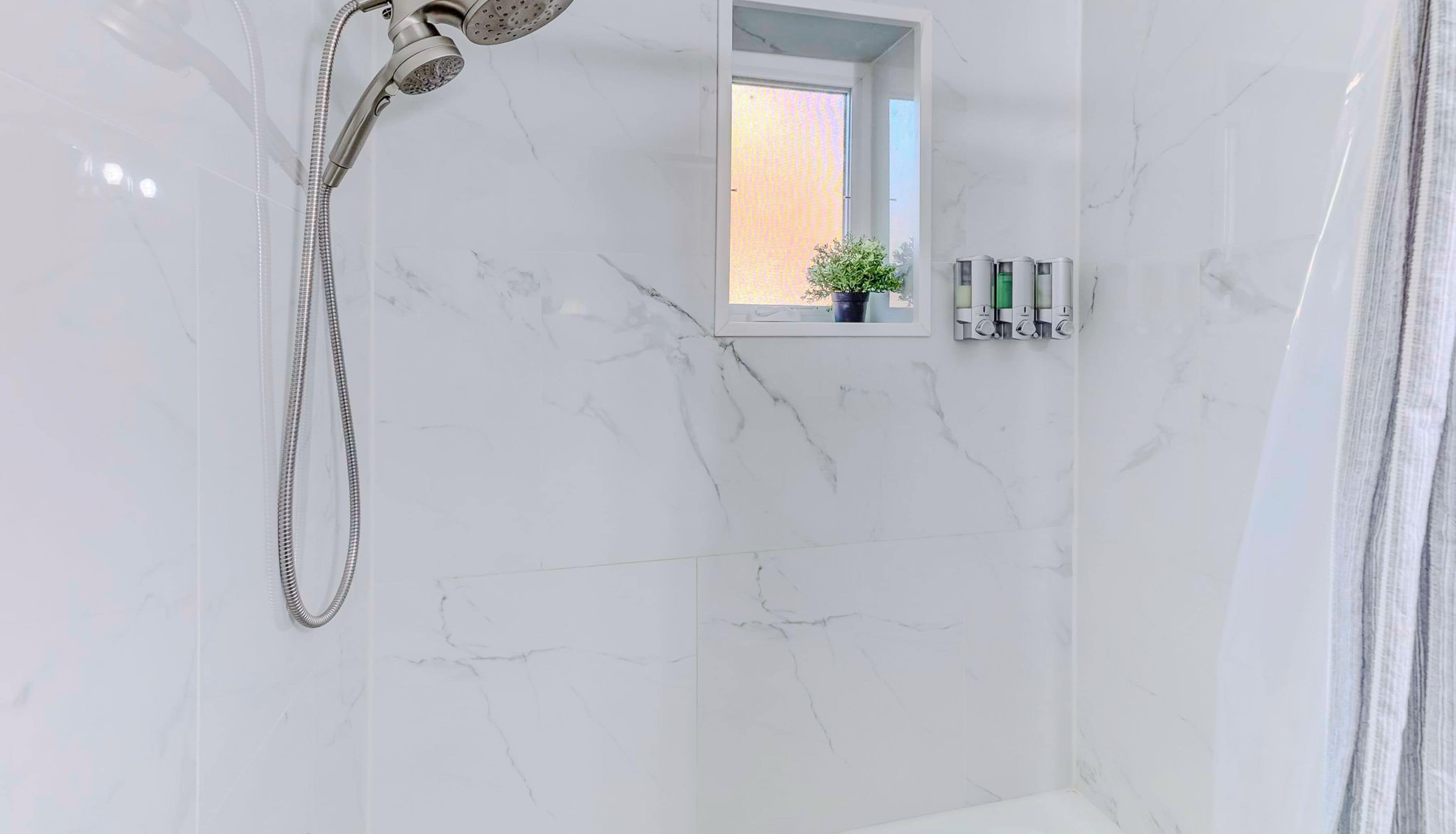 Une salle de bain avec une douche, une petite fenêtre ornée d’une plante et des articles de toilette accrochés au mur.