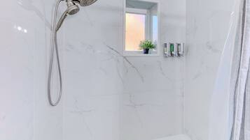 A bathroom with a shower, a small window with a plant, and toiletries on the wall.