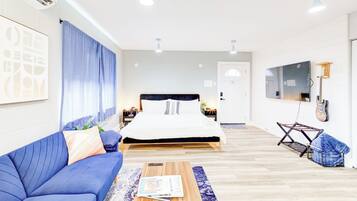 Una habitación de hotel moderna con una cama, un sofá azul, una mesa de centro de madera, un televisor y una guitarra.