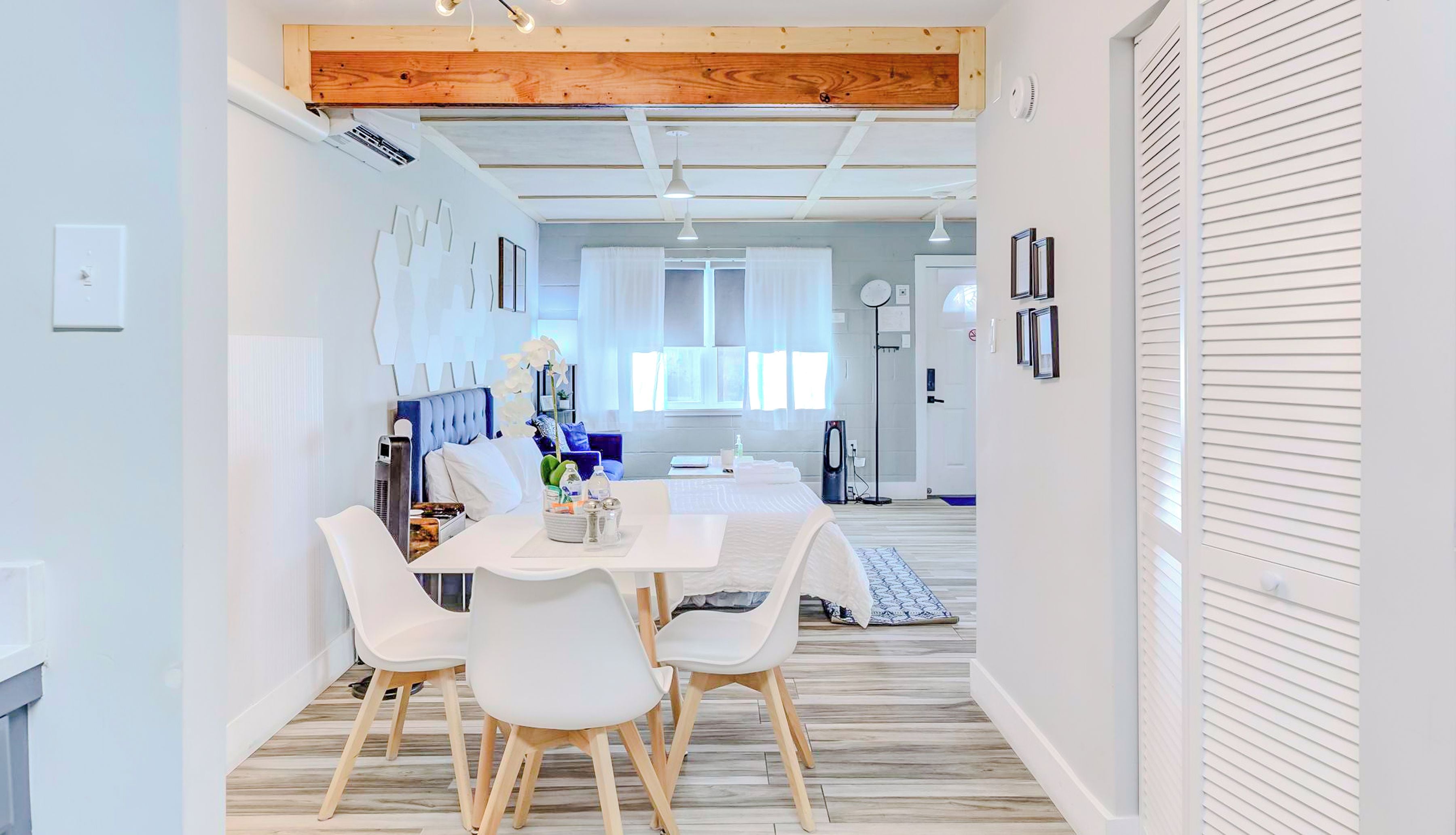 Un espace de salle à manger moderne avec une table et des chaises blanches, une poutre en bois au plafond et des luminaires suspendus.
