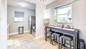 Una cocina moderna con horno empotrado, refrigerador de acero inoxidable y ventana con vistas a la ciudad. Cuenta con una barra con taburetes y una pequeña mesa.