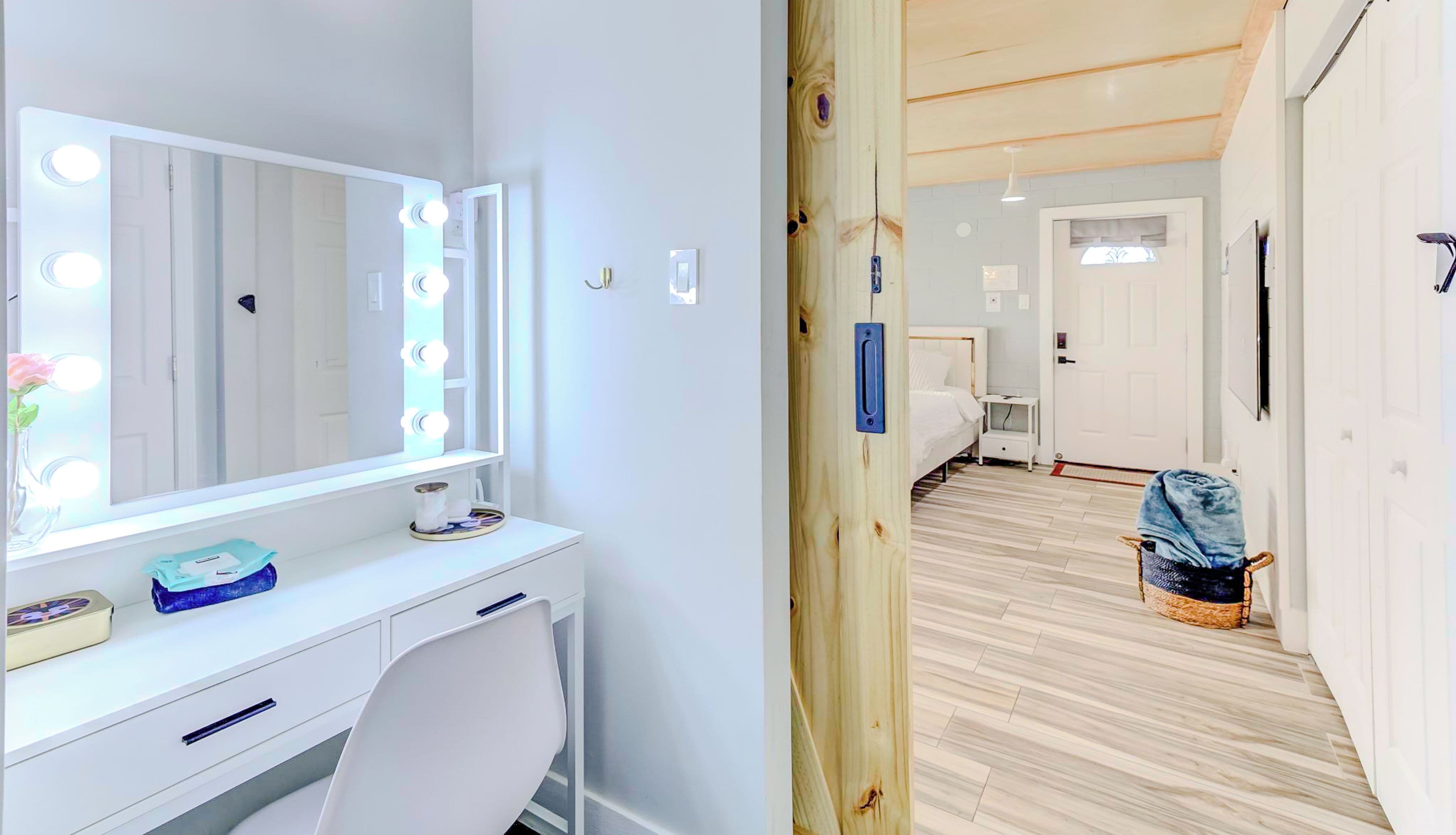 Una habitación con tocador, espejo con iluminación, paredes de madera, cama y un pasillo.