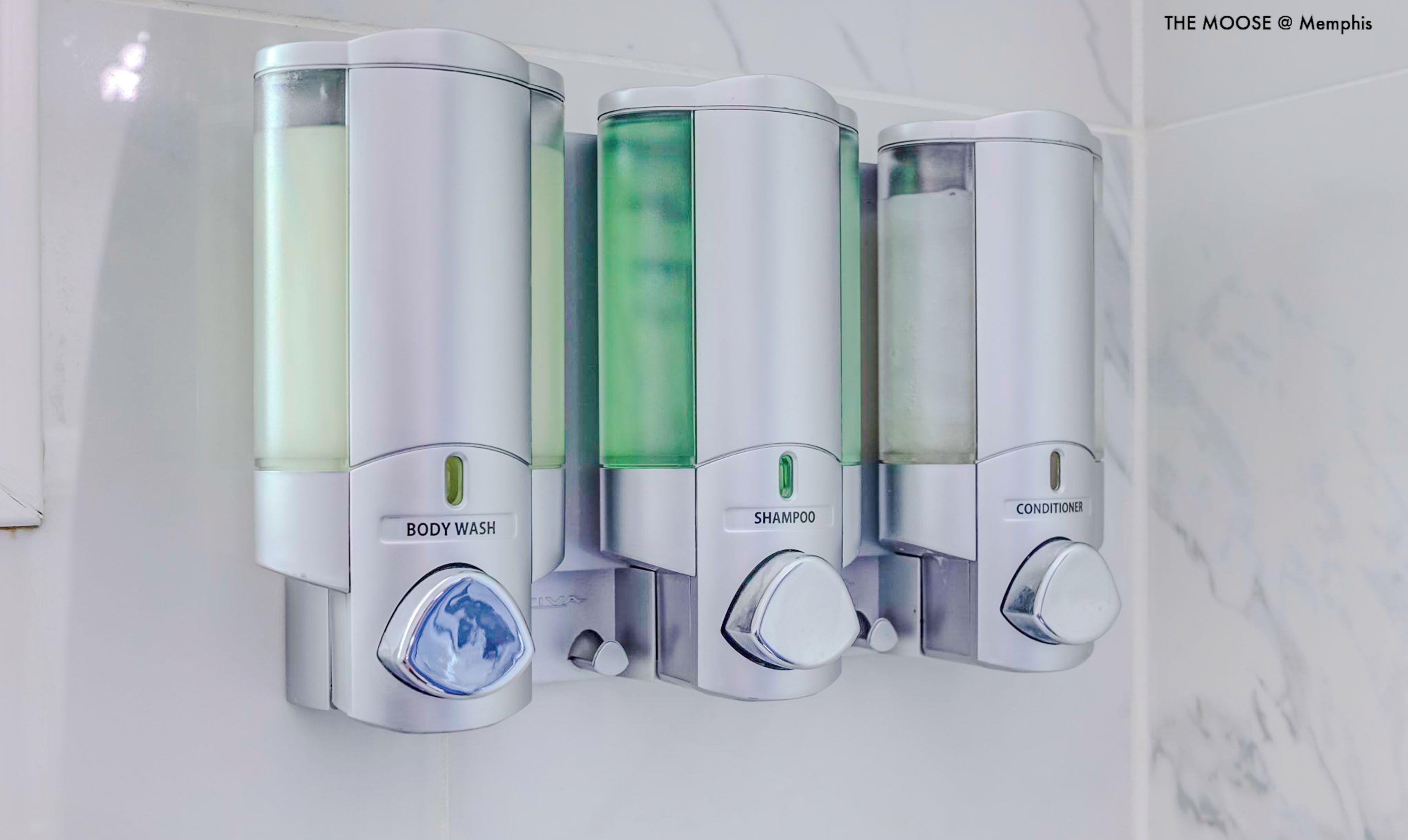 A wall-mounted dispenser with three compartments labeled BODY WASH, SHAMPOO, and CONDITIONER.