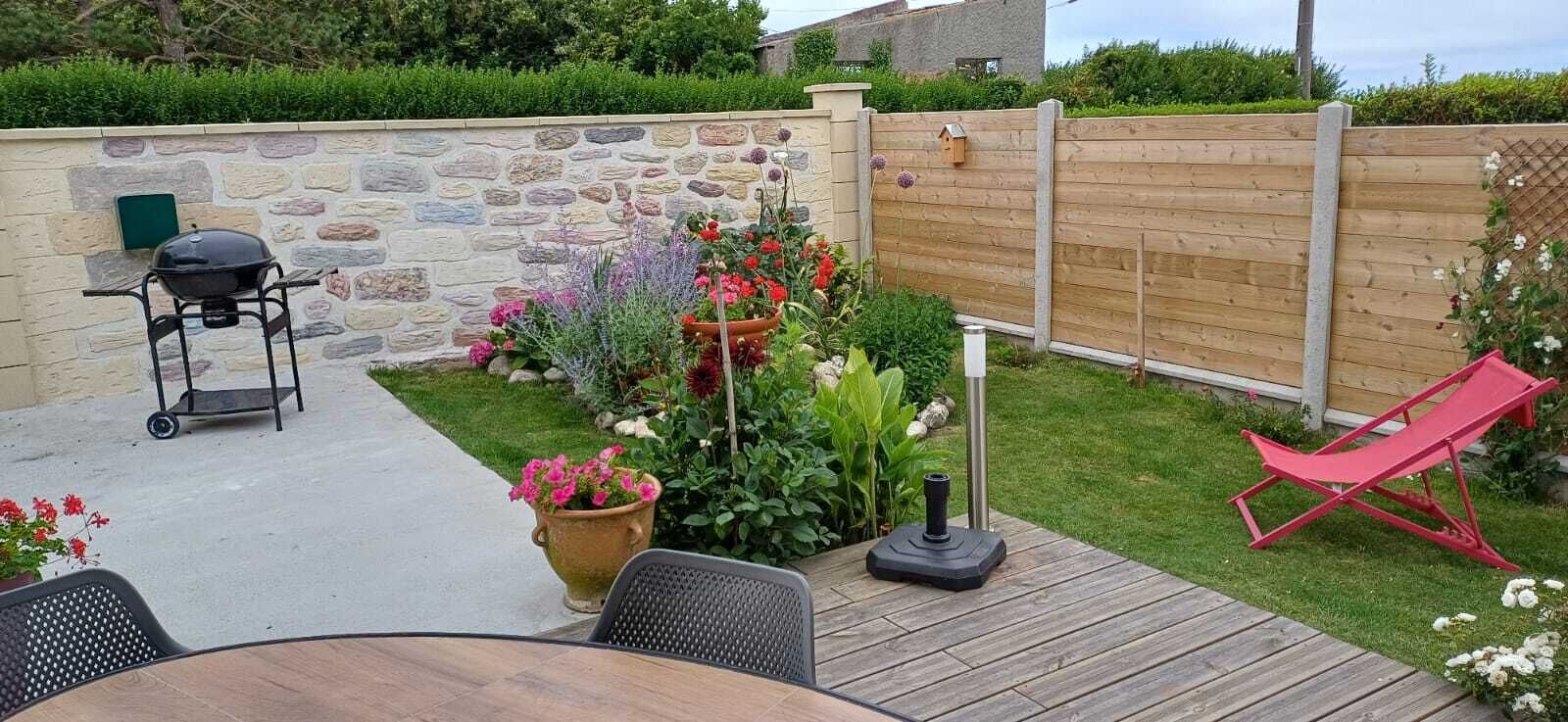 Eine Terrasse mit Tisch und Stühlen, einem Grill, einem Holzboden und einem Holzzaun.