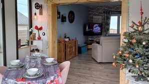Et spiseområde med et bord dækket til fire personer, et juletræ og et fjernsyn i baggrunden.