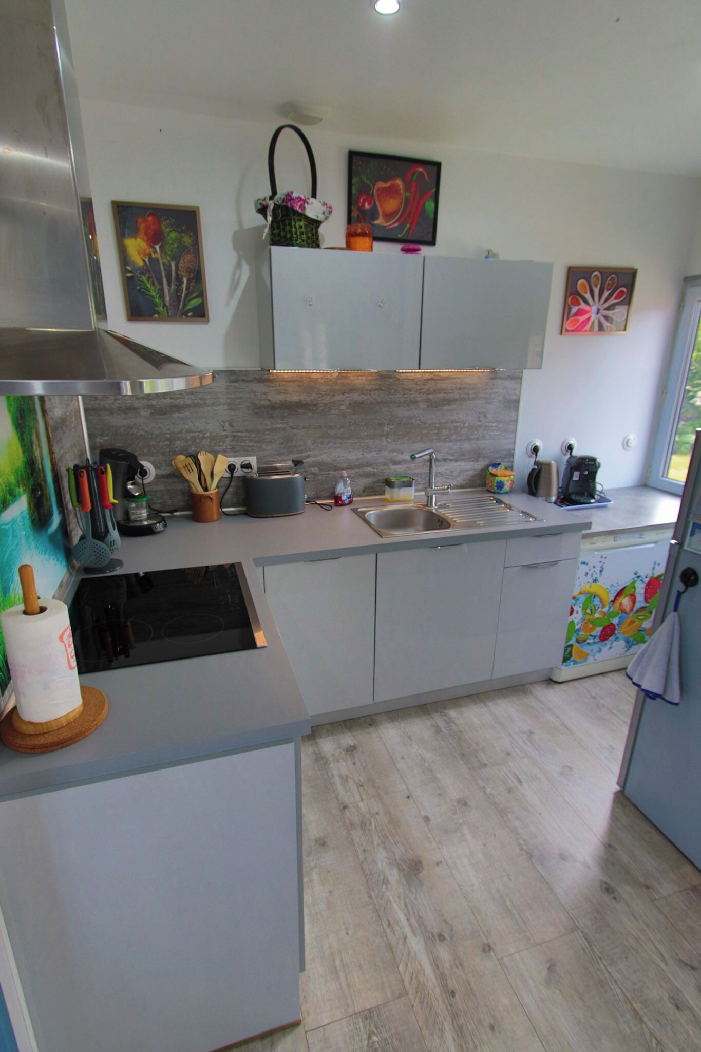 A modern kitchen with a stainless steel range hood, a built-in dishwasher, and a countertop with various kitchen utensils and appliances.