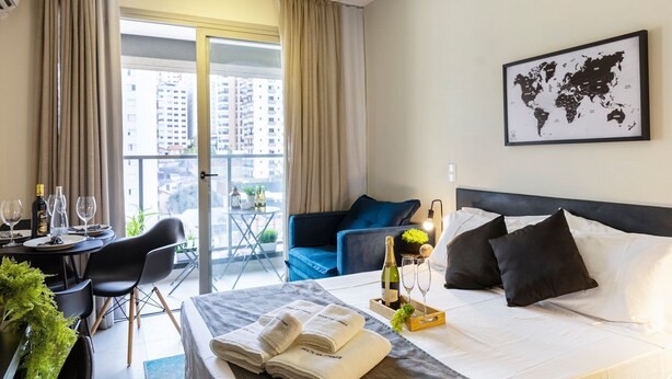 A hotel room with a bed, a dining table with chairs, a balcony with curtains, and a world map on the wall. - Allianz parque AC Solário | Brazilian Corner. (São Paulo)