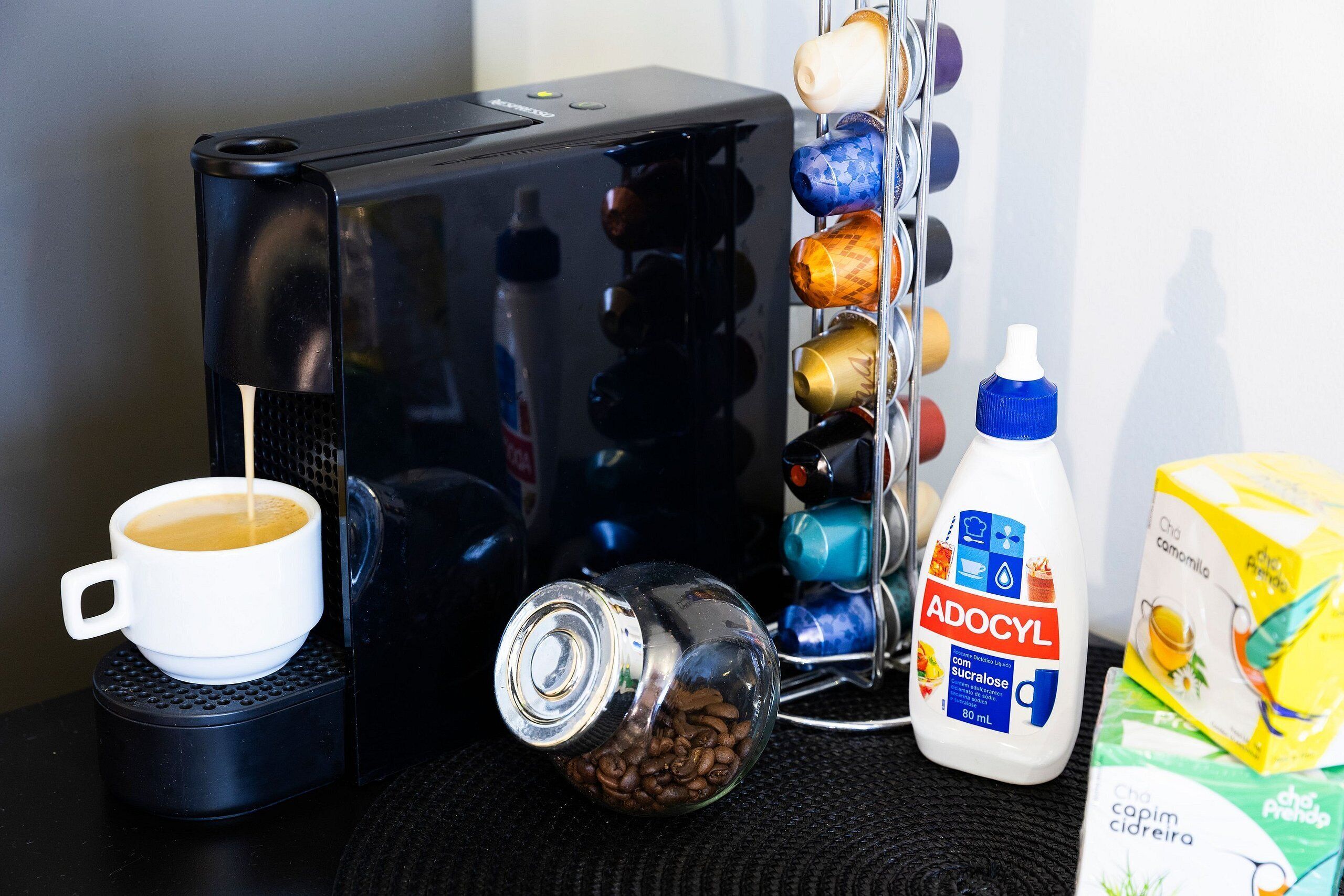 Una màquina de cafè, una tassa de cafè, una ampolla de llet Adocyl i un cartró de Capim Cidreria.