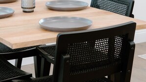 Een eettafel met vier grijze borden, een glas en zwarte stoelen.