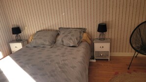 Un dormitorio con cama, dos mesitas de noche con lámparas, una silla y papel tapiz estampado.