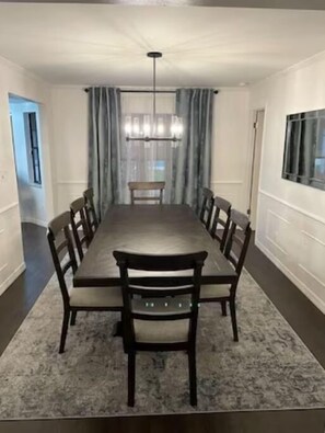 Une salle à manger avec une longue table et des chaises, un lustre et une vue sur l’extérieur.