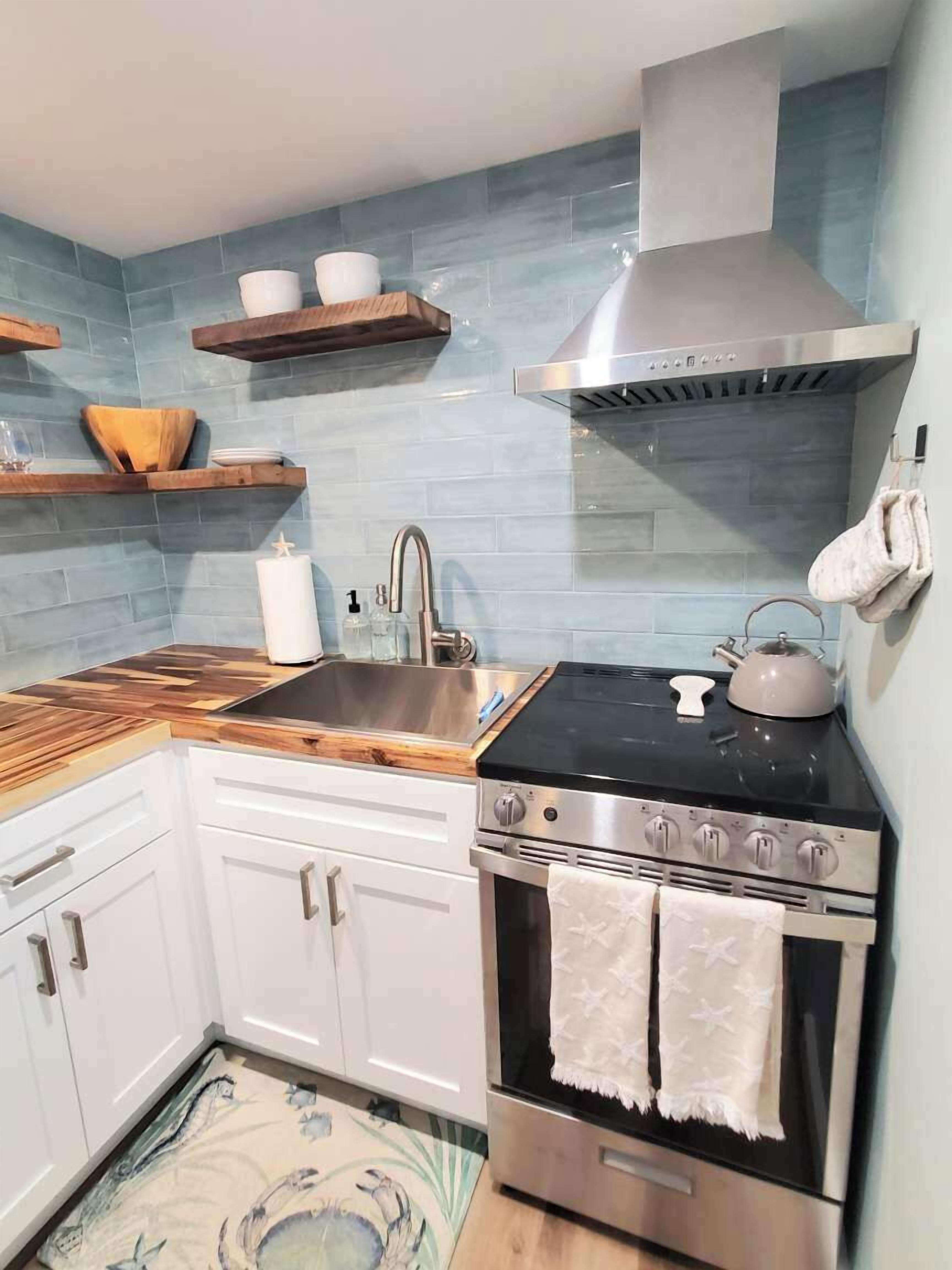 A kitchen with a stove, sink, and wooden shelves.