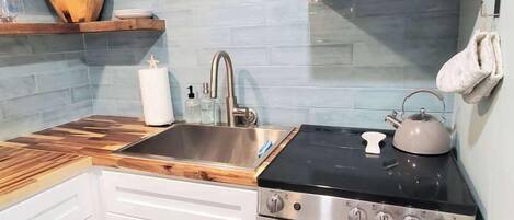 A kitchen with a stove, sink, and wooden shelves.