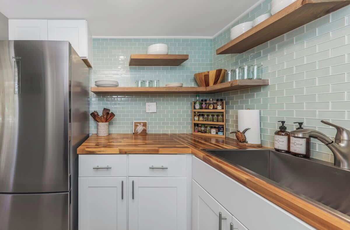 Eine Küche mit Edelstahl-Kühlschrank, Holz Arbeitsplatten, weißen Schränken und einer hellblauen gefliesten Spritzschutzleiste.