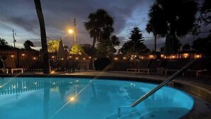 A swimming pool with a curved edge, surrounded by palm trees and lounge chairs. - Heated Pool! Steps 2 beach! Luxurious King bed (Indian Rocks Beach)