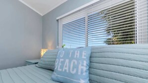 A bedroom with a bed, a pillow with 'TO THE BEACH' text, and a window with blinds. - Heated Pool! Steps 2 beach! Luxurious King bed (Indian Rocks Beach)