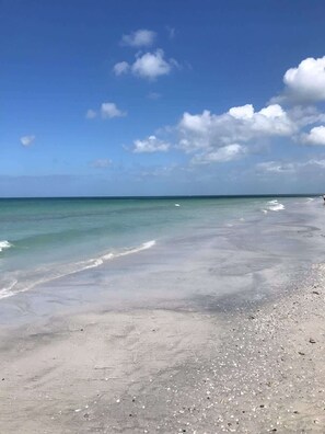 A beach with clear water, a sandy shore, and a person walking.