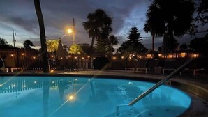 A pool with a curved edge, surrounded by palm trees and a fence. - Coral Reef~90° Heated Pool~Remodeled~2 min 2 beach (Indian Rocks Beach)