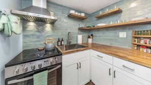Une cuisine moderne équipée d’une cuisinière, d’un four et d’une hotte en acier inoxydable. On y trouve des étagères en bois au-dessus du plan de travail, ainsi qu’une variété d’ustensiles et de récipients de cuisine sur le plan de travail.