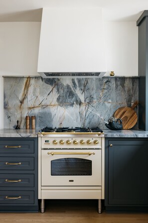 A kitchen with a white stove, dark cabinets, and a marble backsplash. - New! Beautiful Beach House Steps from Sunset Cliffs!  (San Diego)