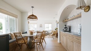 A modern kitchen with wooden cabinets, a dining area with a round table and chairs, and a large window providing natural light. - New! Beautiful Beach House Steps from Sunset Cliffs!  (San Diego)