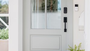 A white door with a glass panel, a doorknob, a small potted plant, a doormat, and a wall-mounted light fixture. - New! Beautiful Beach House Steps from Sunset Cliffs!  (San Diego)