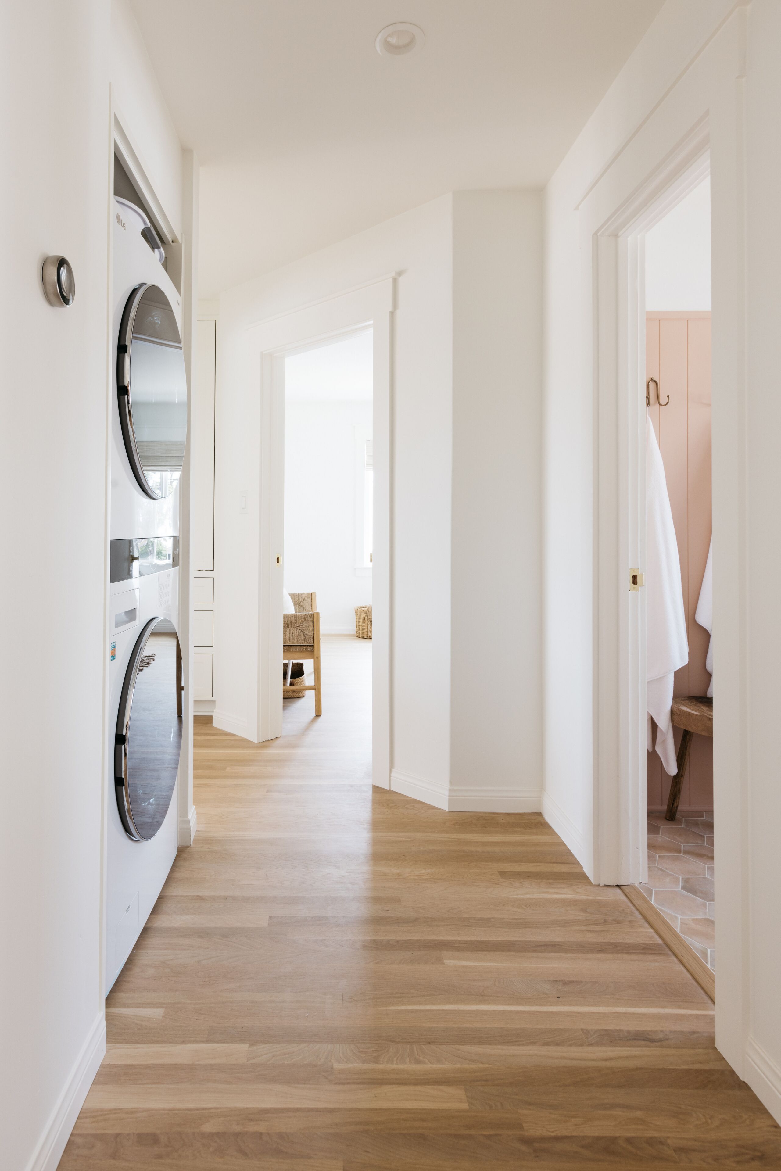 Un couloir avec un lave-linge, un plancher en bois et une porte donnant sur une salle de bain.
