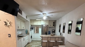 A modern kitchen with white cabinets, a dining area with a table and chairs, and a beige sofa with a pillow. - Casa Caracol, Apartamento Totalmente Equipado Para su Estancia en San Carlos Son (San Carlos Guaymas)